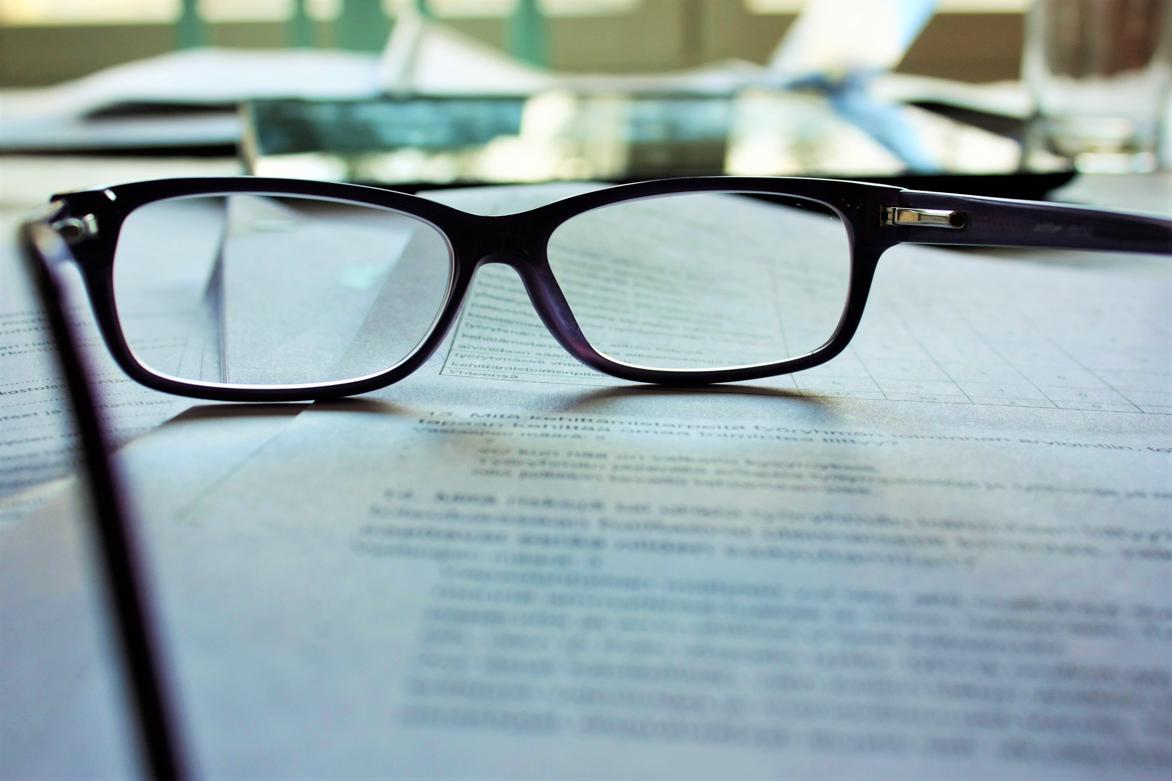 A stack of documents and papers with a pair of reading glasses on top