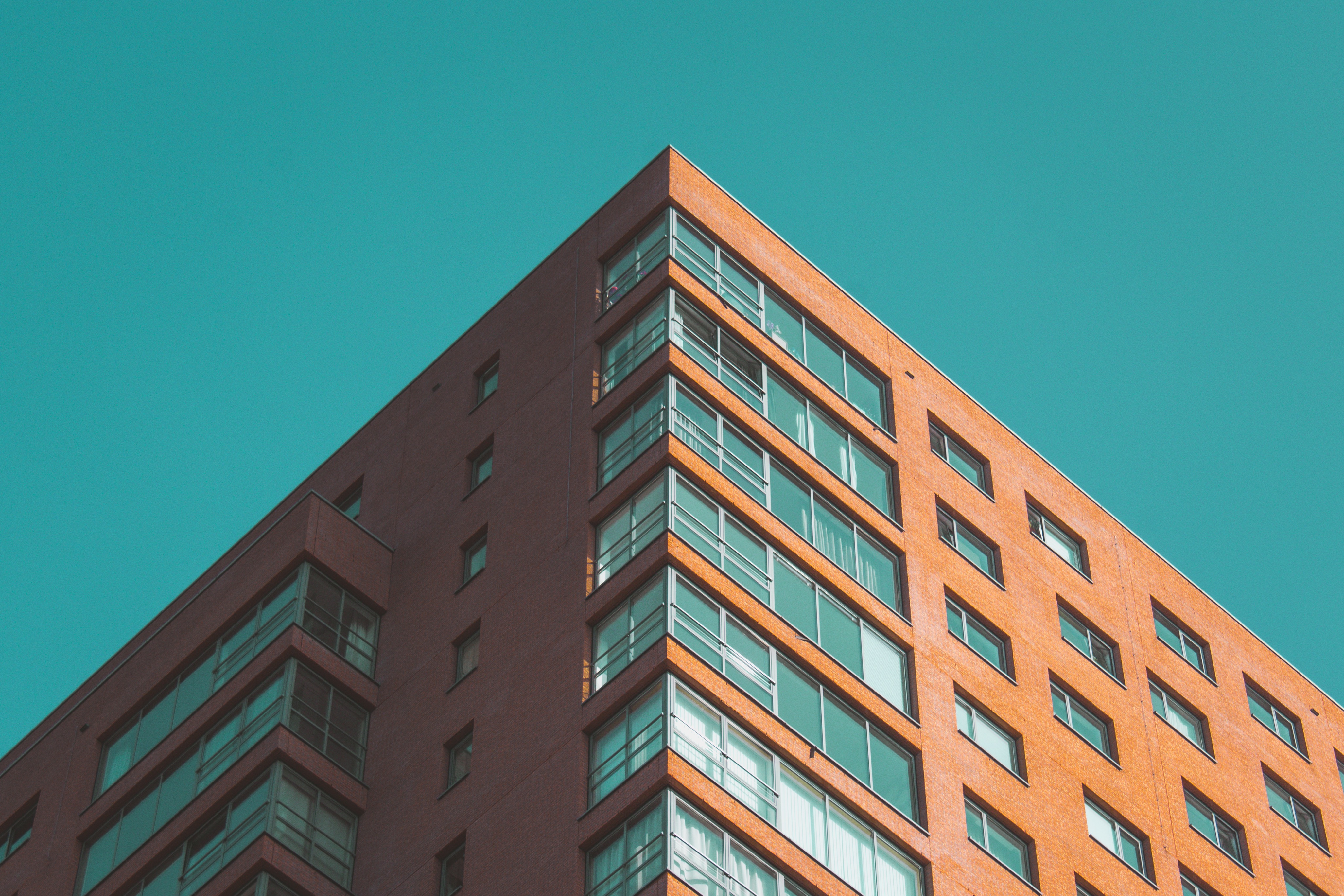 A tall, modern brick and glass building with a teal sky behind it