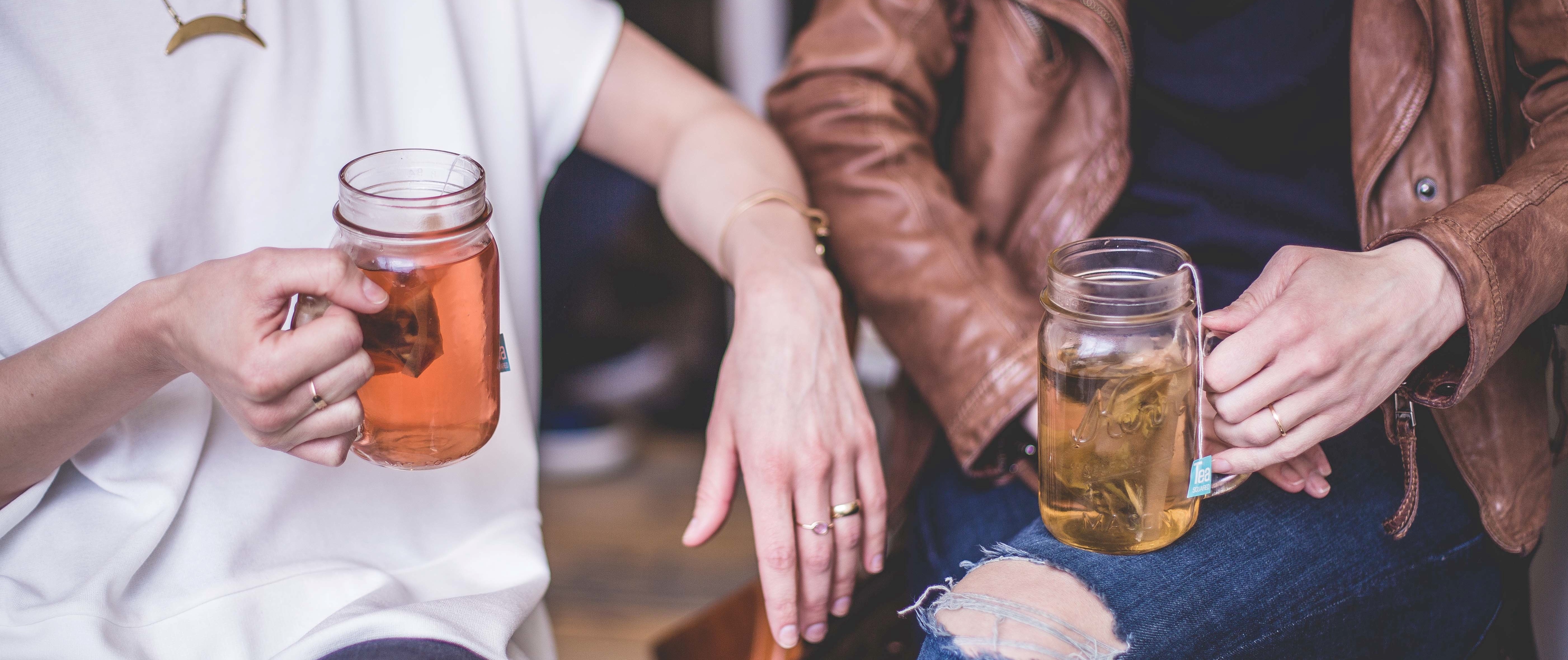 Two women chatting whilst drinking mason jars of herbal tea