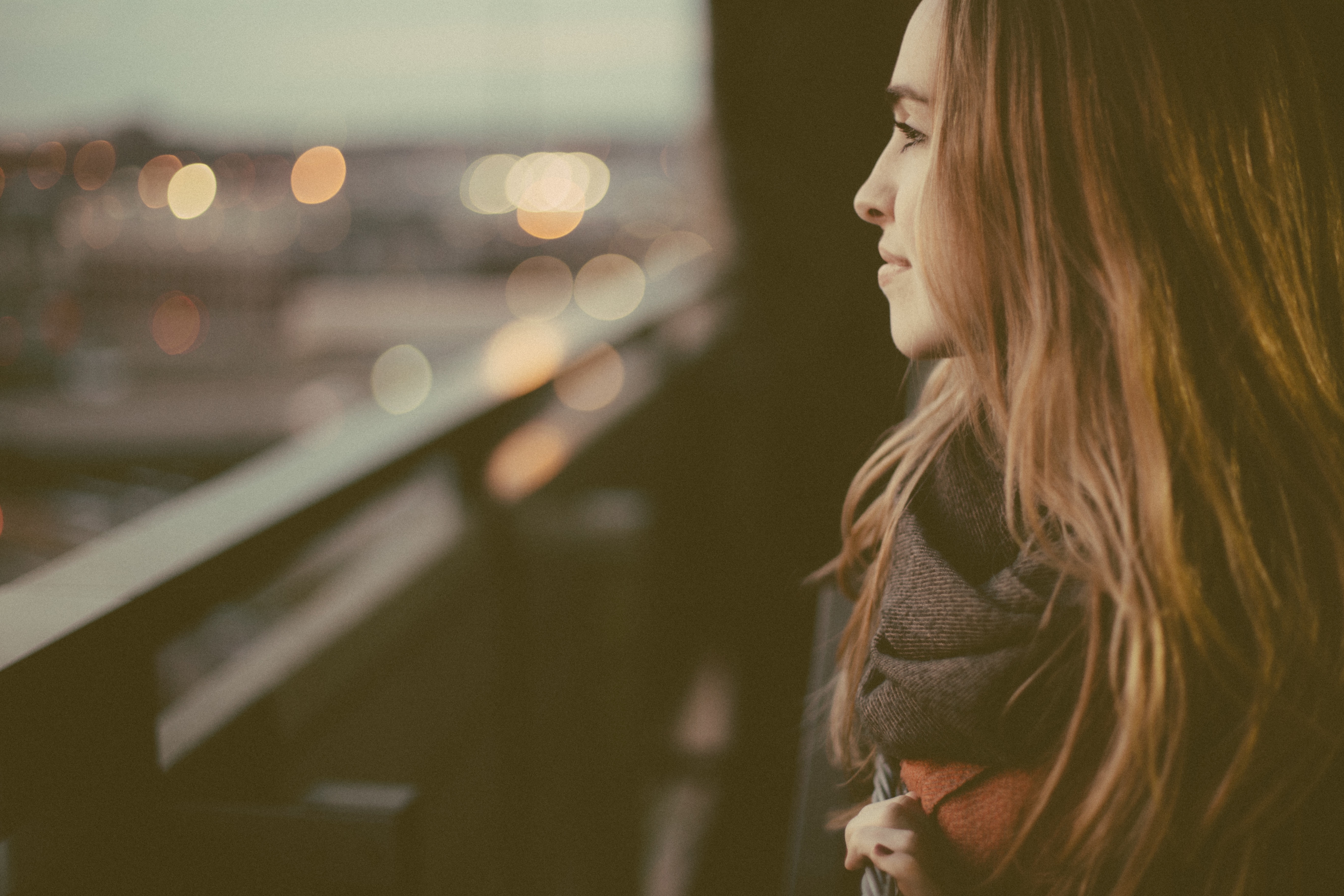 A woman in the foreground smiles as she looks out over am out of focus cityscape 