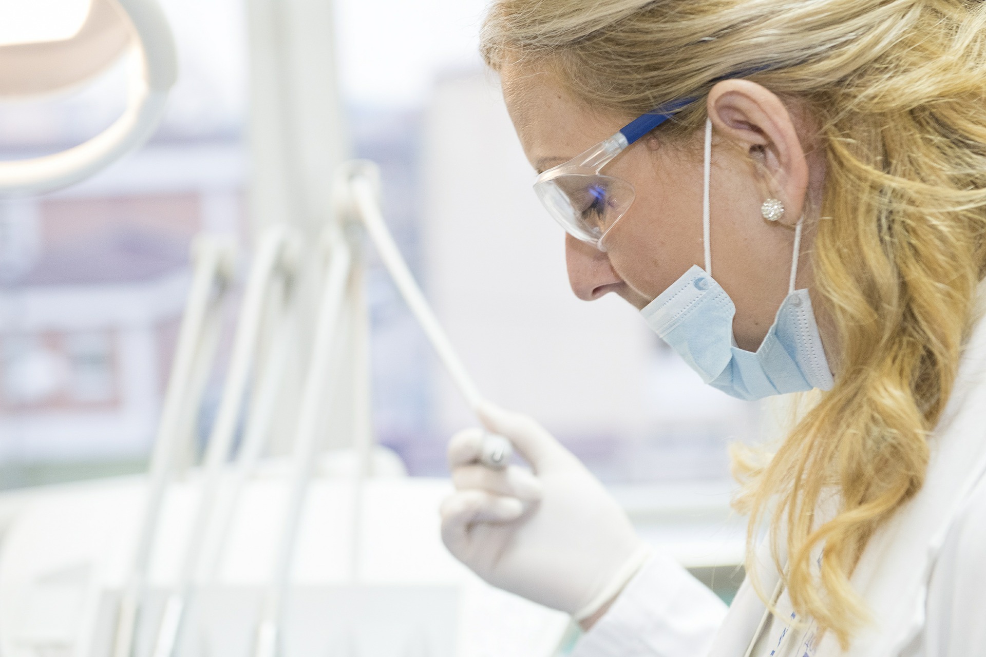 A lab assistant holding a swab wearing a face mask and eye protectors