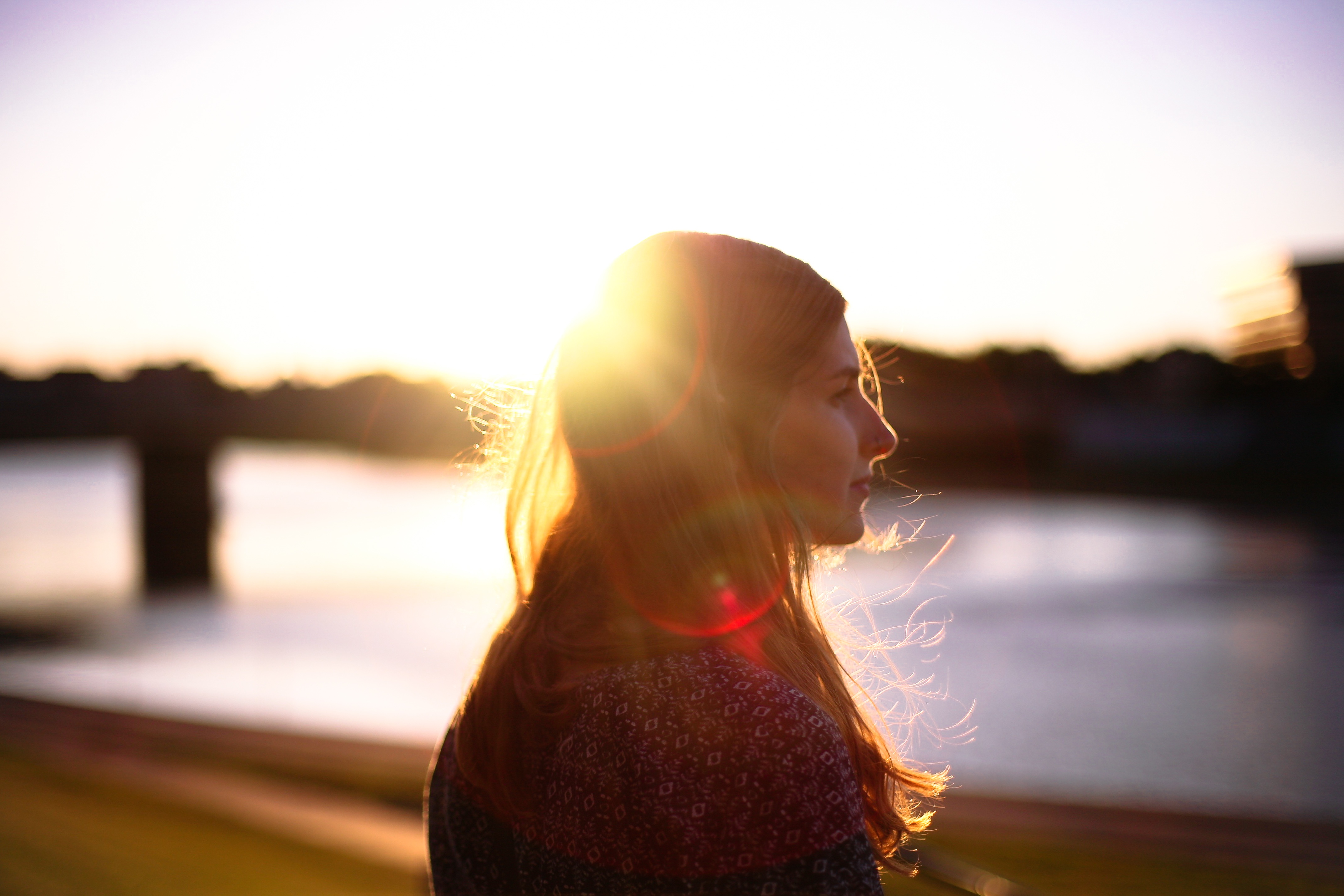 A young woman looks over a river at sunset with a bridge in the background