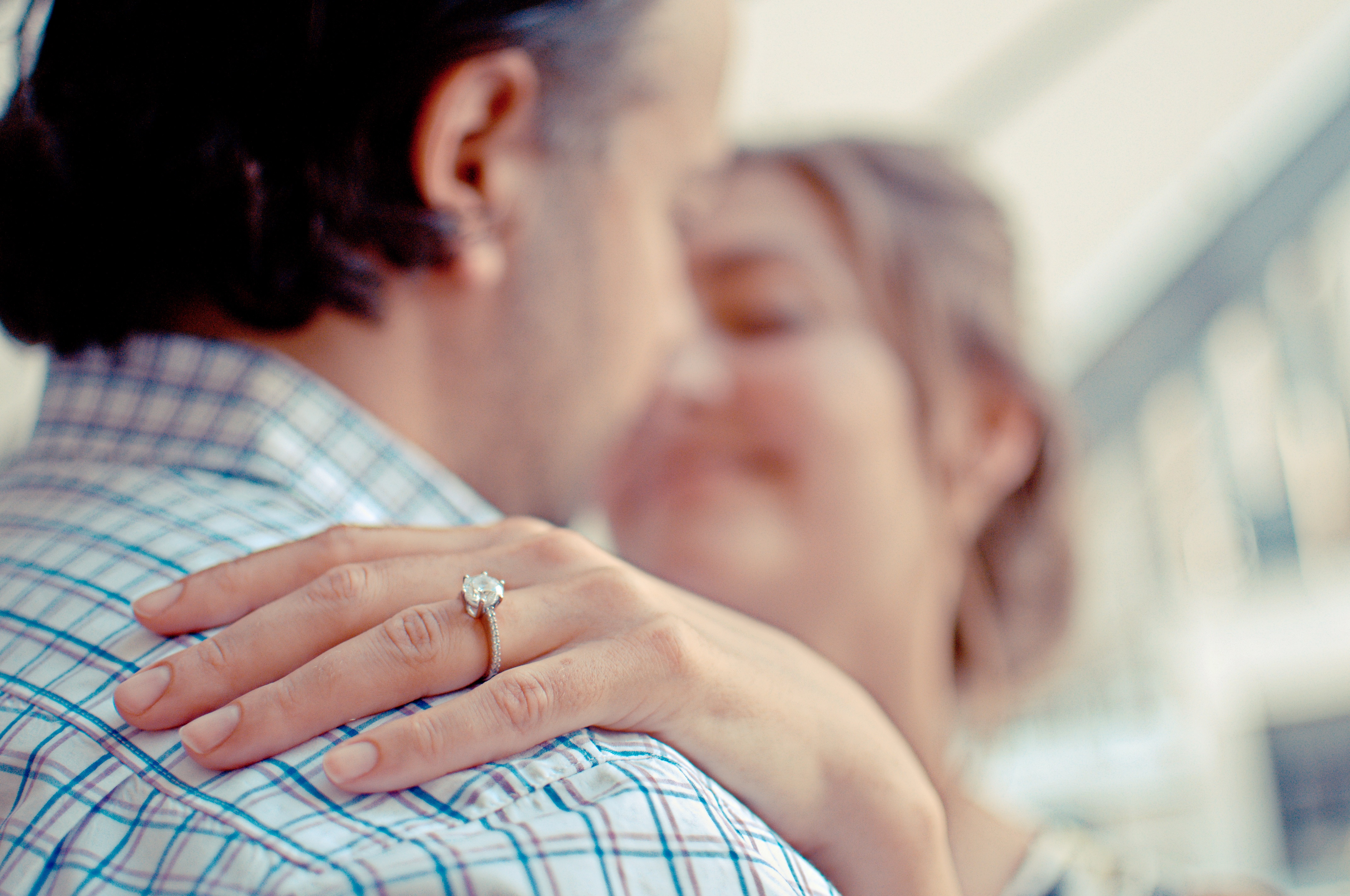 A couple embrace, one of them is wearing an engagement ring which is the focus of the shot