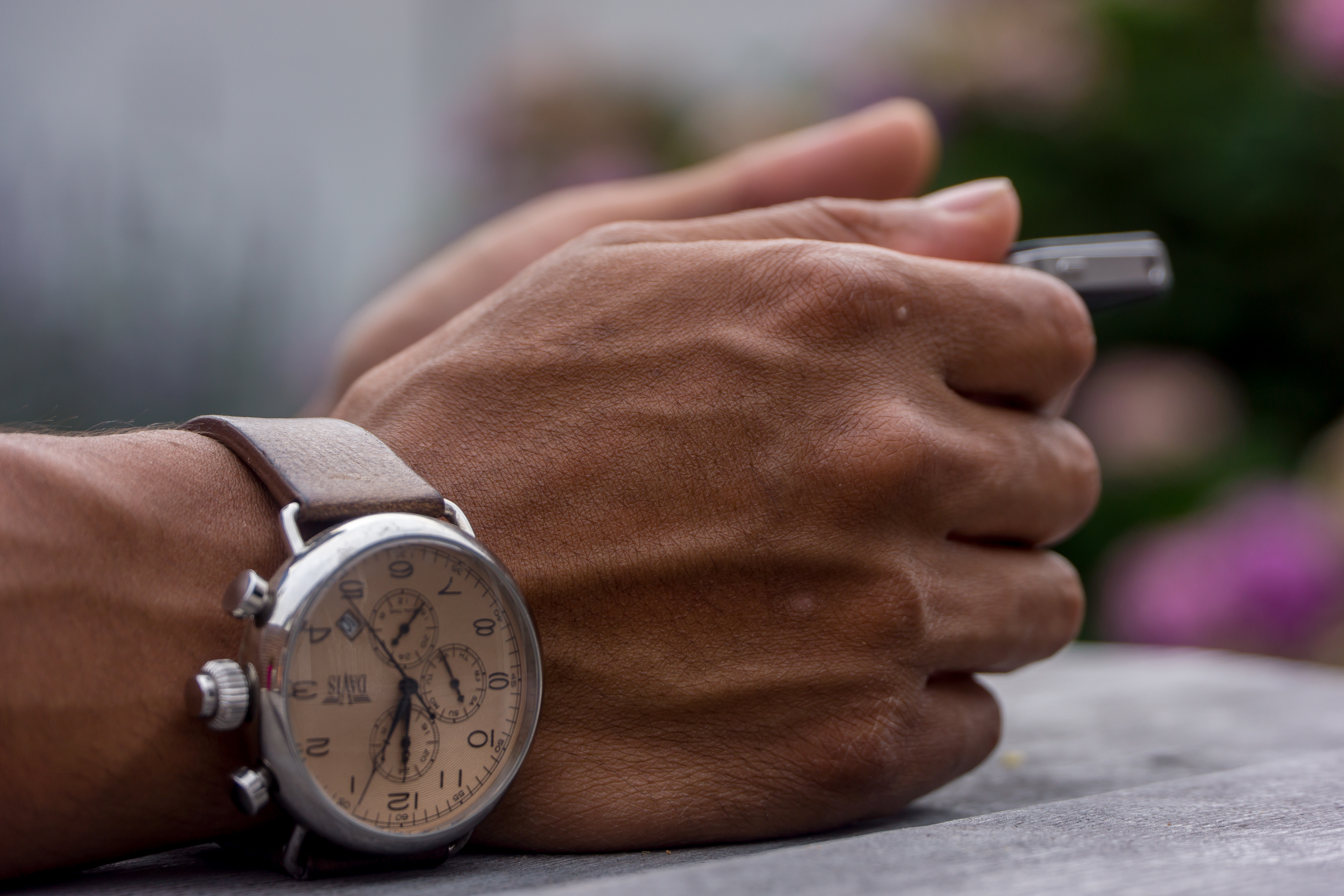 someones hands restingon a table holding a pen with a silver watch with brown leather strap on his wrist