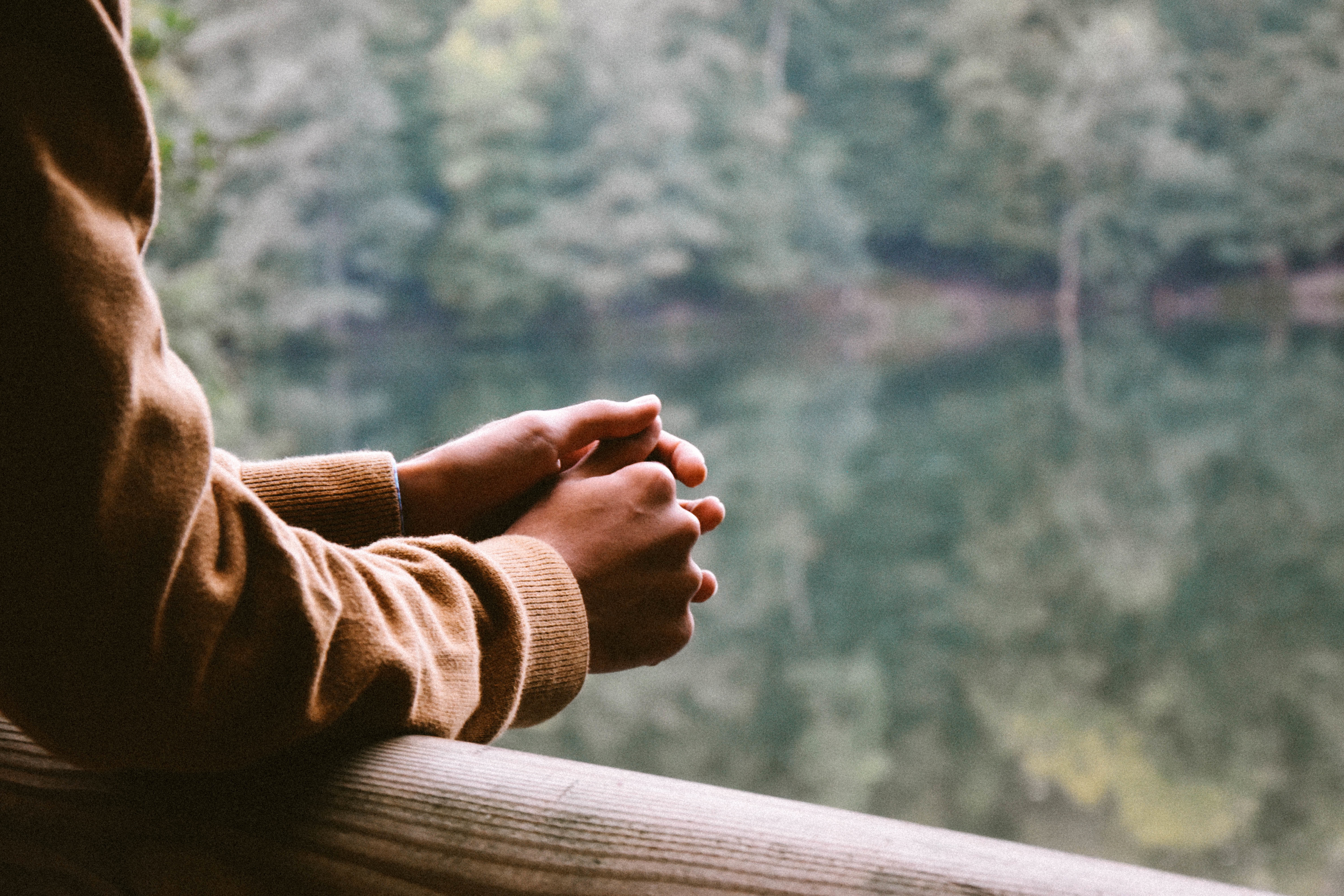 A persons arms rest on a wooden fence as they look out over a lake