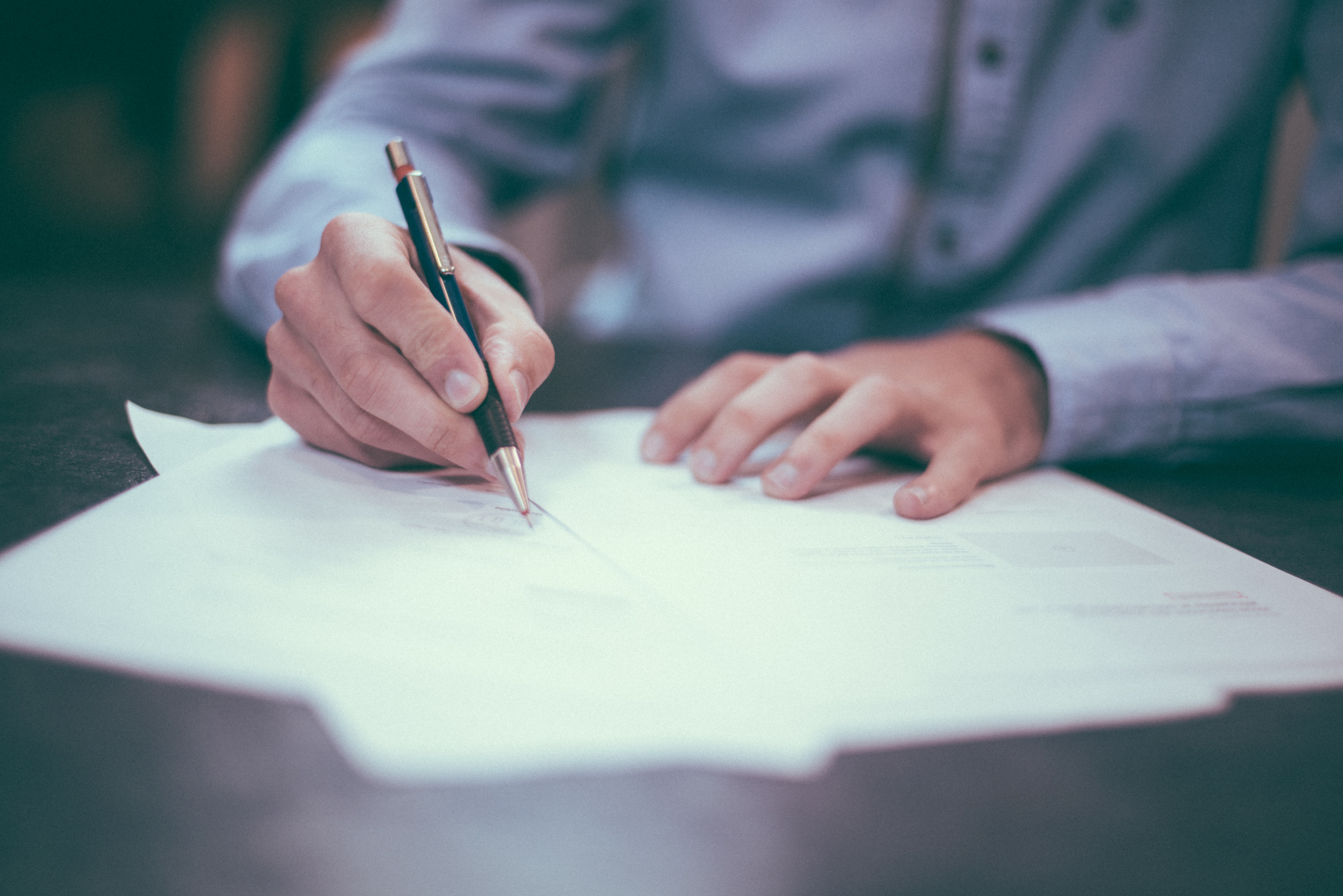 a person in a blue shirt fills out some forms on a dark table