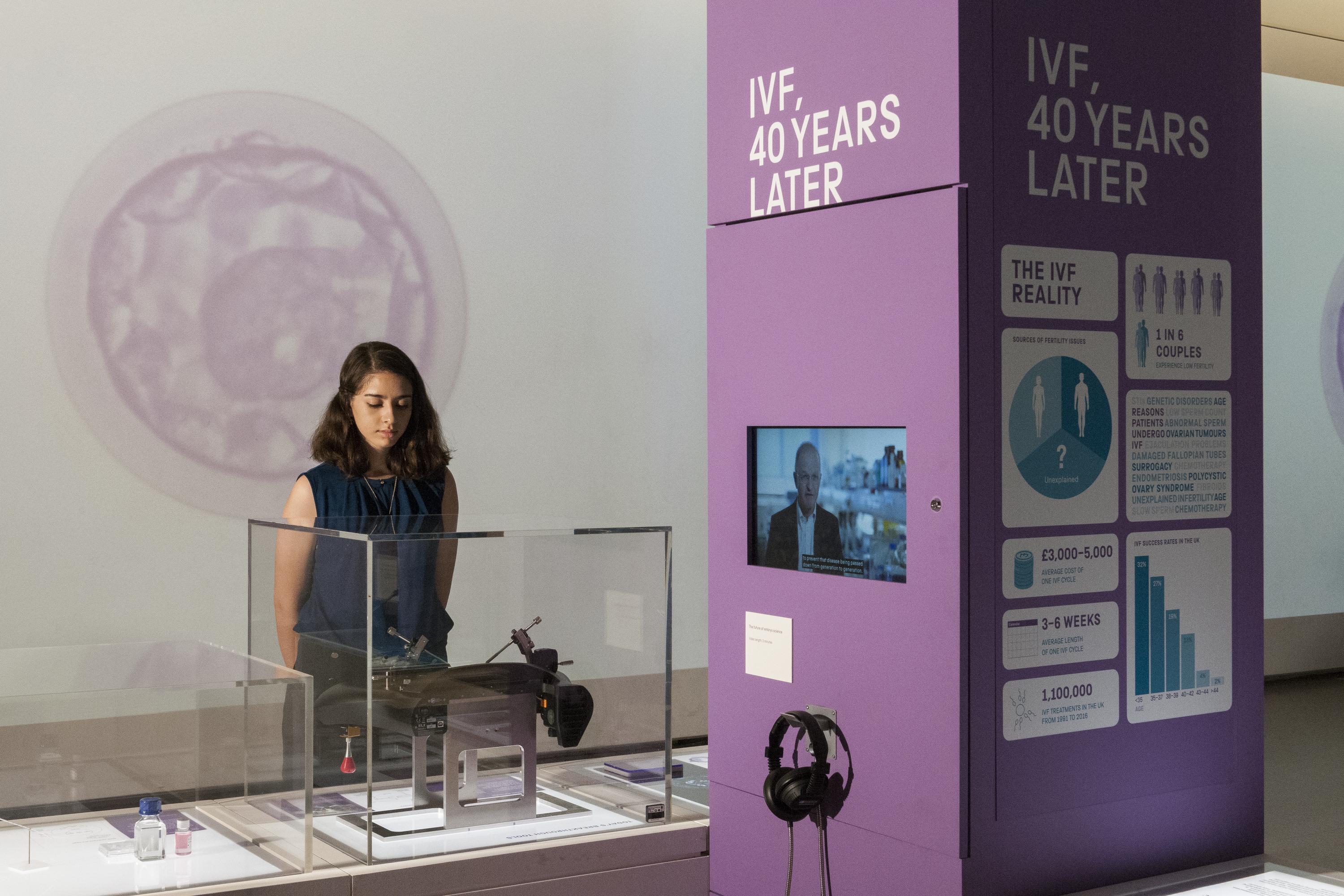 A woman examines a piece of medical equipment on display at the Science Museum's exhibition. Next to here is a column displaying various statistics with the title 'IVF, 40 years later'